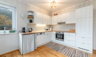 A modern kitchen with white cabinets and wooden surfaces. The space is bright and inviting, with a warm wooden floor and a carpet.