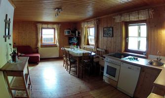 A cozy kitchen with wooden paneling and a dining area. The decor is simple and inviting, with natural light streaming through the windows.
