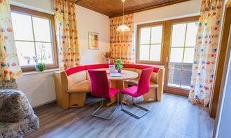 A cozy dining area with a round table and red chairs. Large windows provide plenty of daylight.