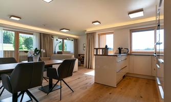 A modern apartment with a light-filled living and dining area. Large windows offer a beautiful view and wooden flooring creates a cozy atmosphere.