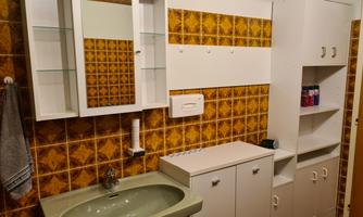 A bathroom with a green washbasin and white furniture. The walls are decorated with orange tiles.