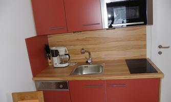 A modern kitchen with red cabinets and a wooden countertop. There is a sink, a microwave, and a coffee machine.