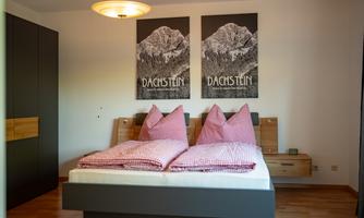 A cozy bedroom with a double bed and checked pillows. Two pictures of the Dachstein mountain landscape hang on the wall.