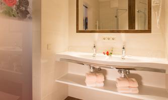 A modern bathroom with a large mirror and a double sink. The floor is made of wood and fresh towels are ready.