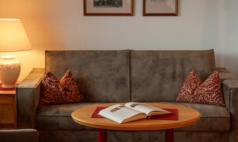 A cozy living room with a gray sofa and cushions. On the coffee table lies an open book, and the walls are decorated with pictures.