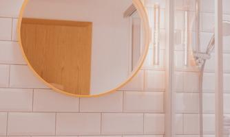 A modern bathroom with a round mirror and a shower. The walls are tiled with white tiles, and there is an elegant sink station.