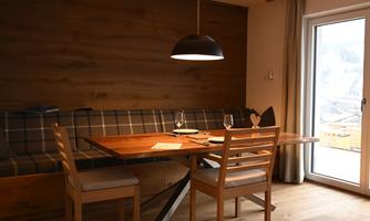 A cozy dining area with a wooden table and chairs. A large window front provides plenty of daylight.