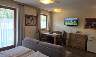 A bright and modern room with a sleeping area and a living area. There is a table with chairs and a television on the wall.