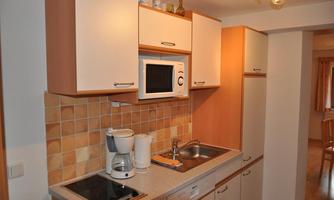 A modern kitchen with wooden cabinets and elegant tiles. It is equipped with a cooktop, a microwave, and a coffee maker.