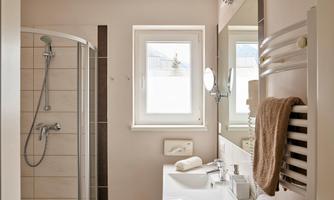 A modern bathroom with a shower, a sink, and a large mirror. Bright walls and a window provide plenty of light.