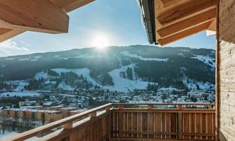 A sunny view from a wooden terrace overlooking snow-covered mountains. The idyllic landscape features a clear blue sky.
