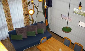 A cozy living room with a blue couch and a large wooden table. Colorful curtains hang on the walls and decorative lamps gently illuminate the space.