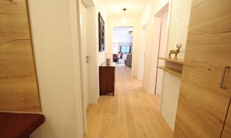 A bright hallway with hardwood floors and simple walls. In the background, a cozy living area is visible.