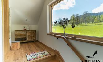 An inviting entrance area with wooden flooring and a large window showcasing a green meadow landscape. A rug with the inscription "Welcome" gives the room a friendly atmosphere.