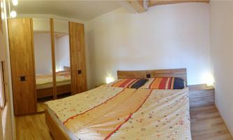 A cozy bedroom with a large bed and wooden furniture. The walls are light and there is a pleasant lighting in the room.
