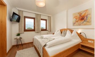 A cozy bedroom with a wooden double bed. Large windows let in plenty of natural light.