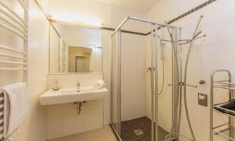 A modern bathroom with a shower and a sink. The walls are brightly tiled and there are towels as well as a towel warmer.