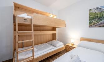 A cozy bedroom with a bunk bed and a single bed. There are wooden details and atmospheric lighting.