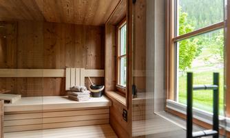 A modern sauna with wooden cladding and a cozy lounging area. The window offers a view of the green landscape outside.