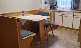 A cozy dining area with wooden furniture and blue cushions. The window lets in plenty of light, and the walls are cheerfully decorated.