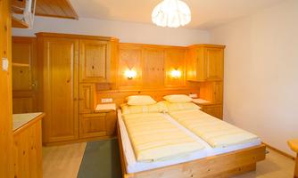 A cozy bedroom with wooden furniture and two beds. The room is bright and inviting, with a simple design and soft lighting.