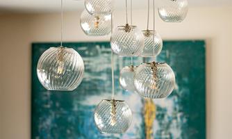 A modern hanging lamp with multiple glass lampshades hangs from the ceiling. In the background, there is a large, artistic painting in shades of blue and green.