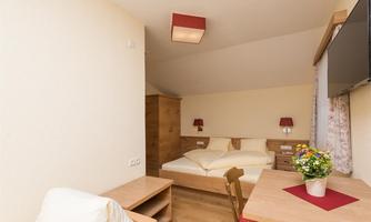A calming room with a double bed and modern furniture. A small table with a flower vase and a television are also present.