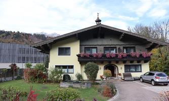 A charming house in alpine style with a beautiful garden. Blooming plants hang on the facade, and a car is parked in the foreground.