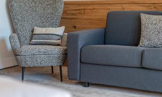 A cozy living area with a gray sofa and a uniquely patterned armchair. The warm wooden elements complement the relaxed atmosphere.
