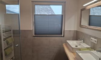 A modern bathroom with two sinks and a large shower cubicle. The window allows plenty of natural light and offers a view outside.