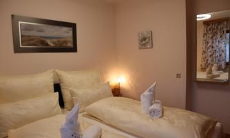 A cozy bedroom with light decor and soft pillows. The warm light accents create a relaxing atmosphere.
