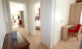 A bright hallway with two open doors. On the right side, there is a table with a red chair.