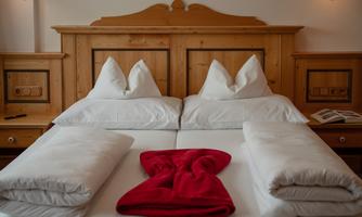 A cozy bedroom with a double bed and white pillows. A red towel is decoratively placed in the center.