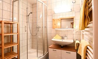 A modern bathroom with a shower cabin and a sink. Wooden shelves and towels give the space a cozy atmosphere.