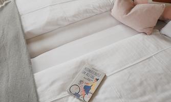 A cozy bed with white sheets and decorative pillows. On the bedspread lies a book.