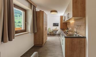 A modern kitchen with wooden elements and bright decor. In the background, a table and a television are visible.