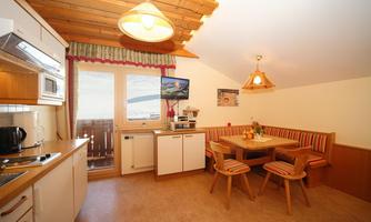A cozy kitchen with wood ceilings and a dining nook. The room is bright and inviting, with windows that let in a lot of light.
