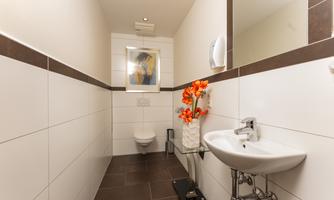 A modern bathroom with a white tiled wall and dark floor. A small plant in a vase and a piece of artwork add a decorative touch to the space.