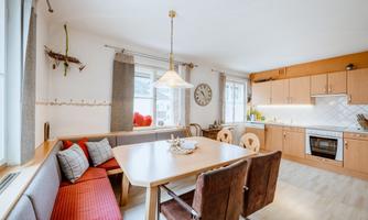 A bright and modern kitchen with a large dining table and a cozy bench. The walls are painted in neutral colors, and there is plenty of natural light from the windows.