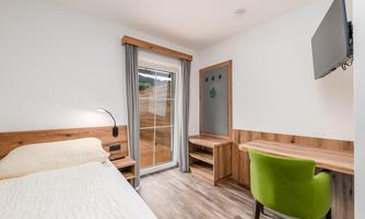 A modern room with a double bed, a desk, and a television. Large windows let in plenty of daylight and offer a view outside.