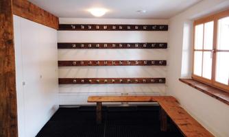 A cozy room with wooden shelves and many hooks on the walls. In the middle stands a long bench.