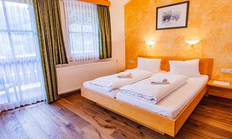 A cozy room with two single beds and wooden flooring. Large windows let in plenty of light and the walls are painted in warm colors.