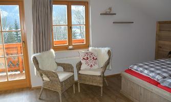A cozy bedroom with two chairs and a window that looks out at the mountains. The decor is bright and inviting.