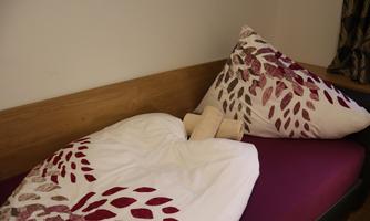 A simple bed with colorful bedding and a pillow. The blanket has a blooming design in beautiful colors.