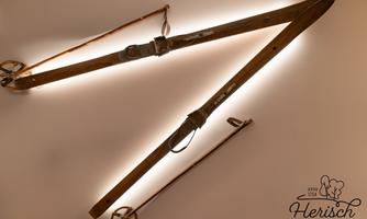 Two old wooden tools hang on the wall, illuminated by a soft light source. They are attached with leather straps and showcase interesting craftsmanship.