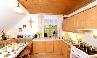 A cozy kitchen with wooden cabinets and a bright atmosphere. Fresh fruits are on the countertop and the windows offer a view of the greenery.