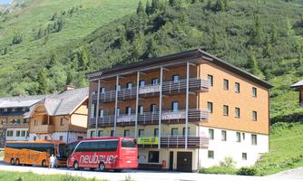 A modern building in the mountains, surrounded by green forests. In front of the house are two buses.