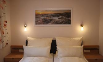 A cozy bedroom with two beds and white pillows. On the wall hangs a picture with an idyllic landscape motif.