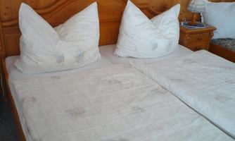 A cozy bedroom with a double bed and large pillows. The bedding is light and kept simple.