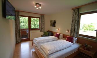 A comfortable bedroom with two single beds and a television. Large windows offer a view of nature and provide plenty of light.